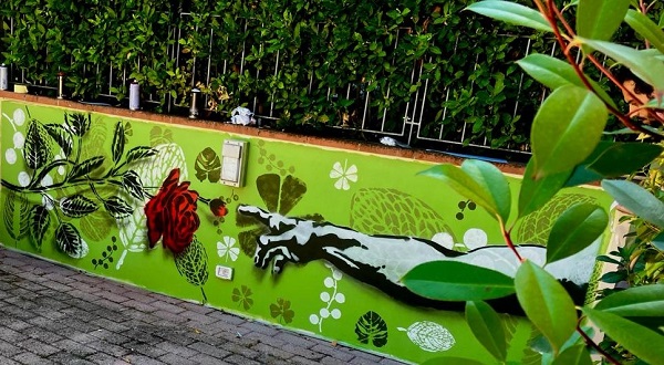 immagine di un murales con sfondo verde e una mano che si avvicina a toccare una rosa